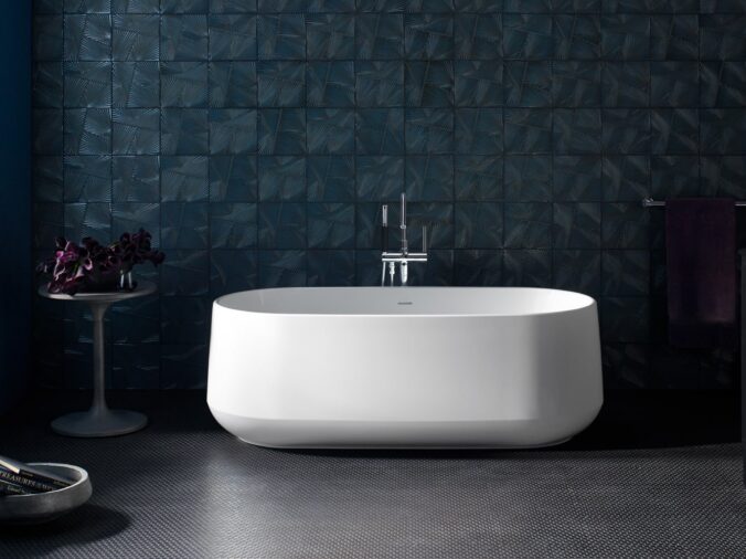 Free standing white bathtub with a darke grey floow and wll behind it