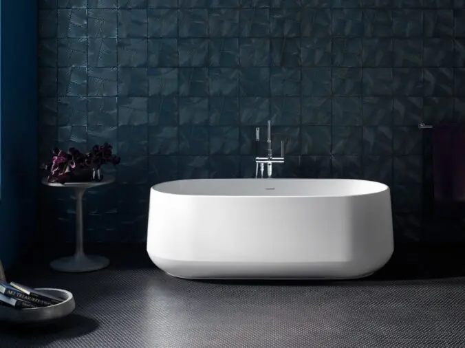 Free standing white bathtub with a darke grey floow and wll behind it